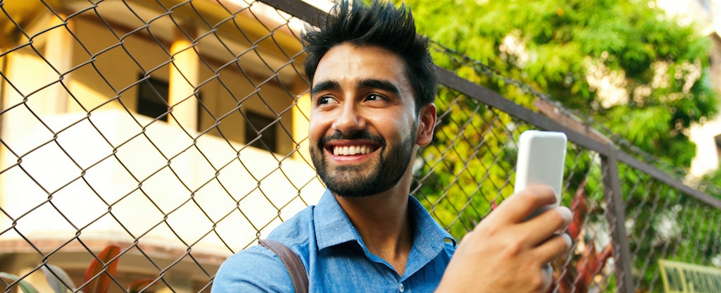 Man standing outside, holding his smart phone and smiling