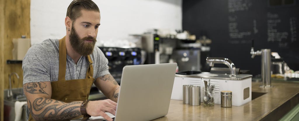 Hipster barista working at laptop in coffee shop