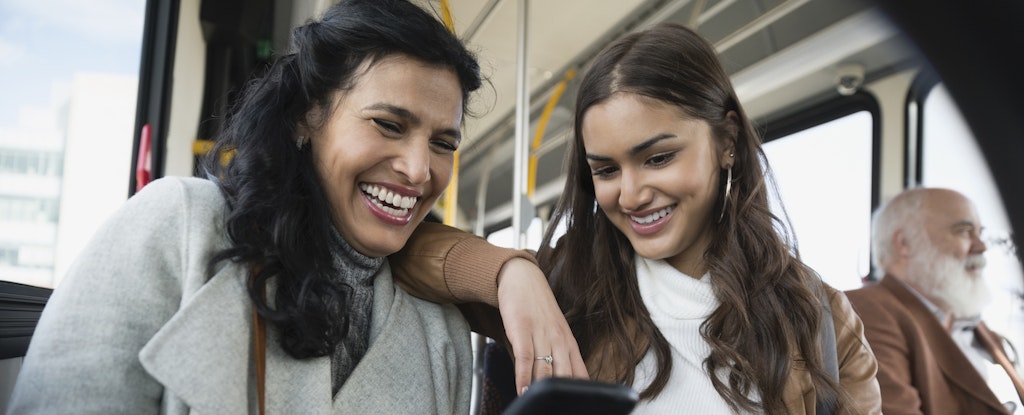 Two women sitting together on a bus, looking at a phone, confident they know what to do with a 1099-R.