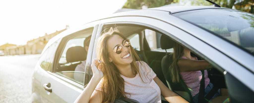 Woman riding in the car with her friends, leaning out of the passenger side window