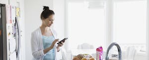 Woman standing in her kitchen, making breakfast and looking at her phone