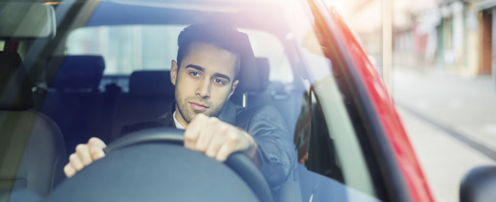 Young man driving car and worried about auto loan debt