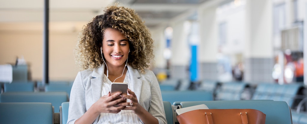 Woman sitting in an airport, looking at her phone and smiling