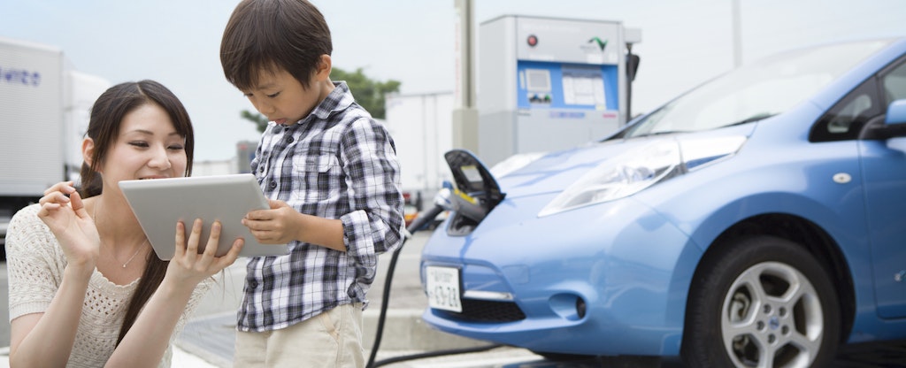 Mom and child using tablet while charging electric car