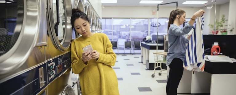 Woman standing in a laundromat, looking at her phone