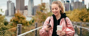 Woman walking in New York, texting on smartphone with one hand and holding a coffee with the other