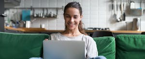 Woman sitting on a sofa, working on her laptop and smiling