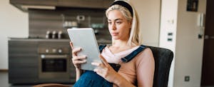 Pregnant woman sitting at home and looking at digital tablet