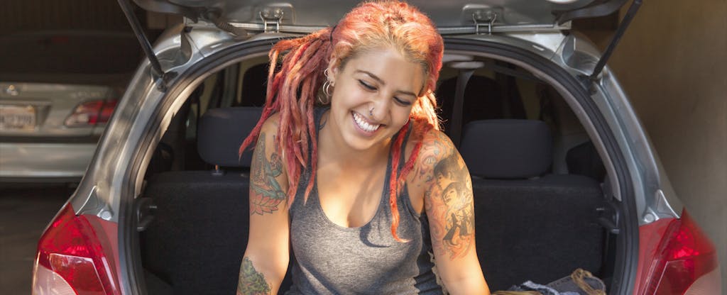 Young woman with pink dreadlocks sitting in trunk of car