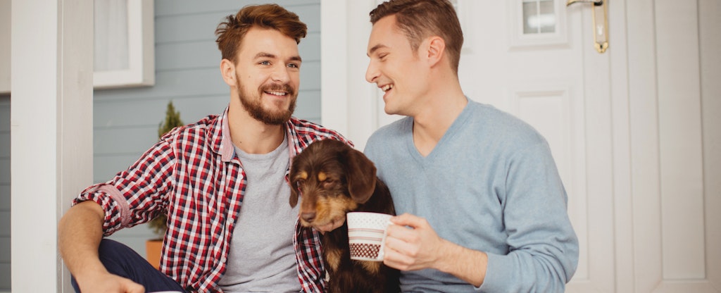 Young same sex couple sitting on porch in front of their home with their dog