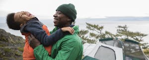 Man and his son hugging each other, laughing, as they're outside camping