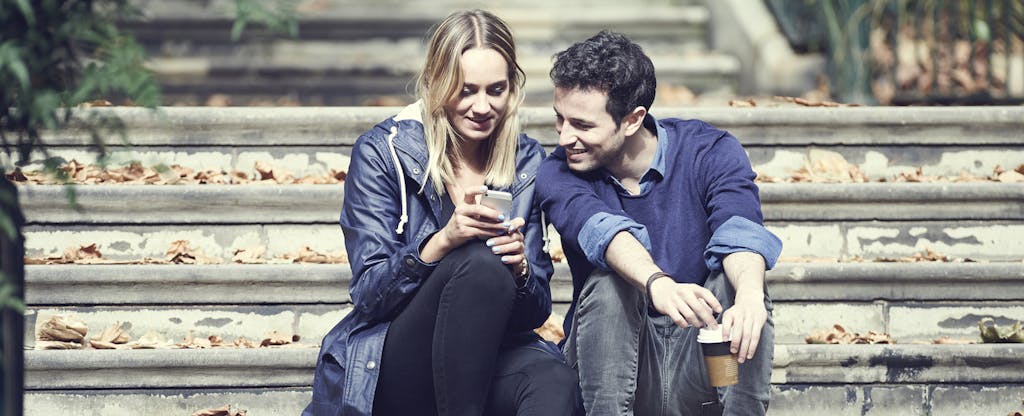 Man and woman sitting together on steps outside, looking at a phone together