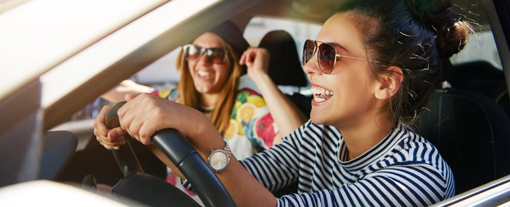Laughing young girlfriends in sunglasses traveling in a car