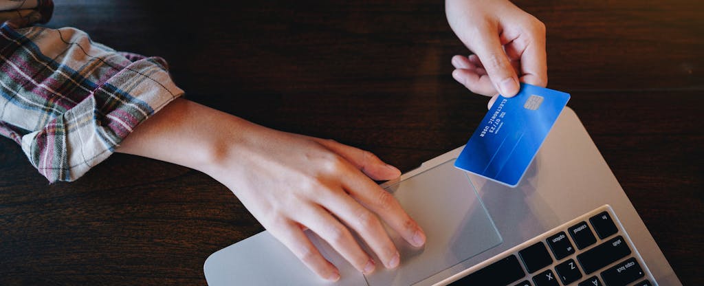Closeup of a person's hands holding a credit card with a laptop open