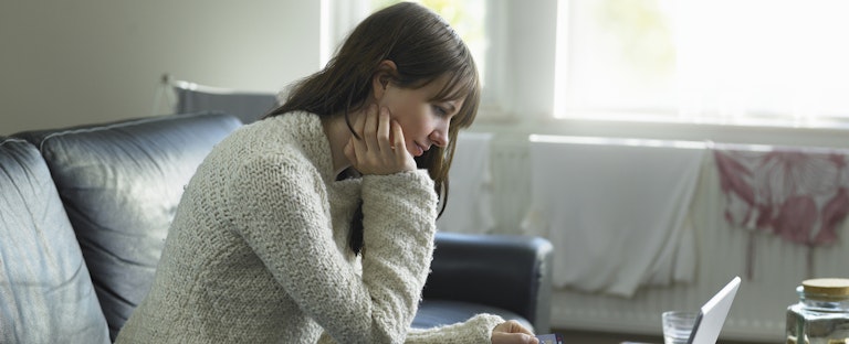 Woman sitting on her couch in her living room, looking at her laptop