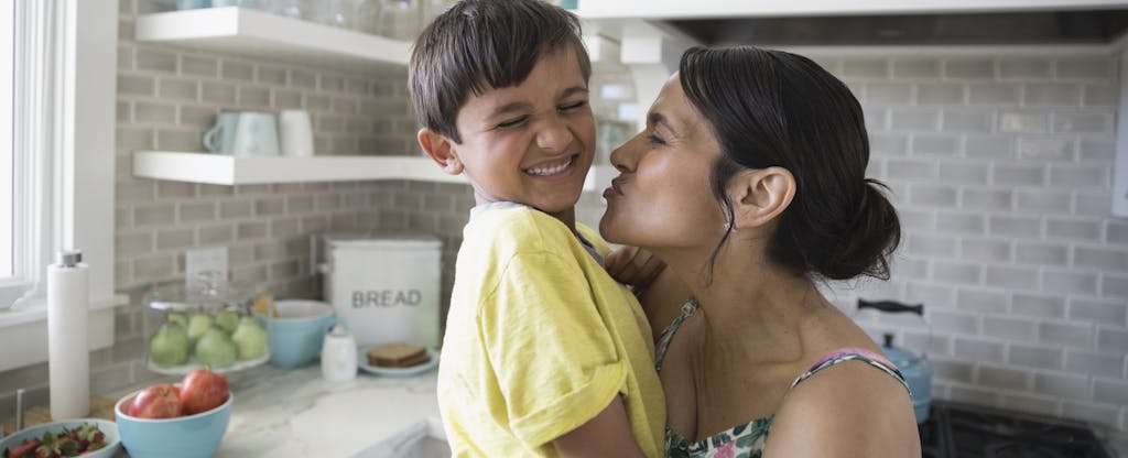 Playful mother kissing laughing son in kitchen