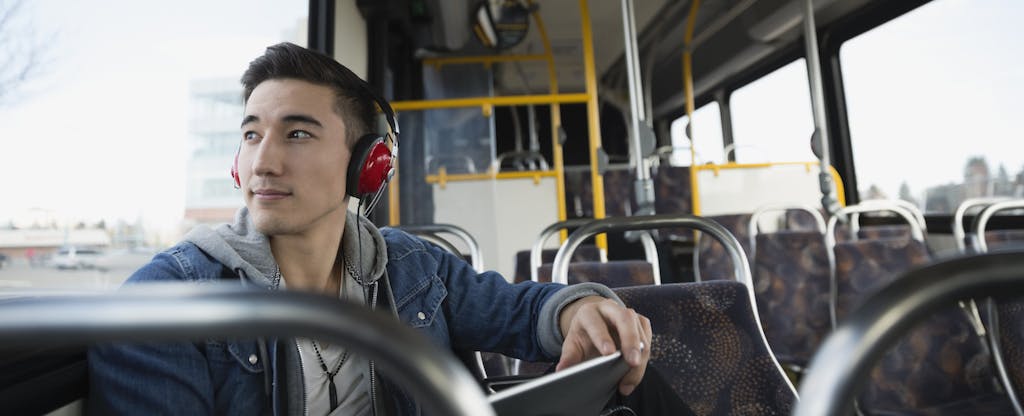 Man sitting on a bus, wearing headphones, holding a tablet and looking out the window