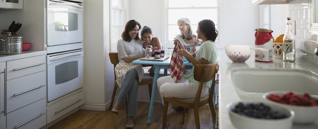 Multi-generational group of female family members gathered in their kitchen, talking and laughing together