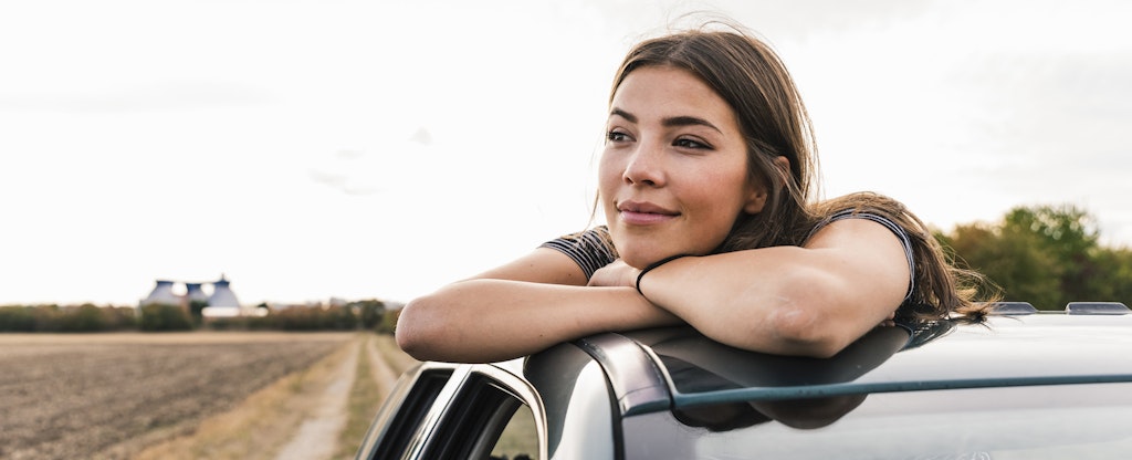 Woman leaning out of the sun roof of her car, thoughtfully looking into the distance