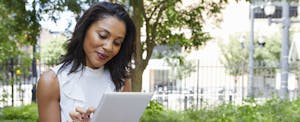 Woman sitting outside in a city park, looking at her tablet and smiling