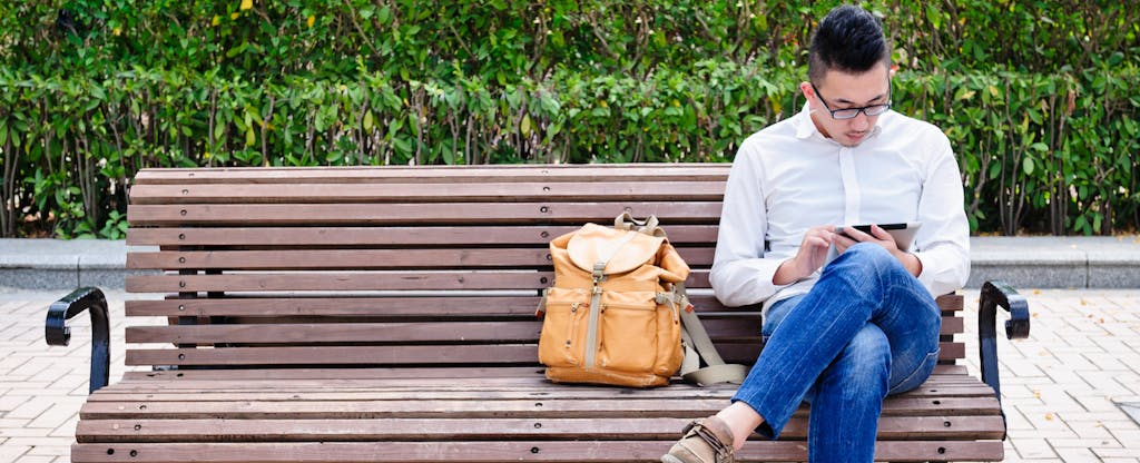 Man sitting on a park bench, reading on his tablet