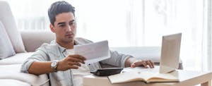 Young man looking at bills and preparing to mail a credit card dispute