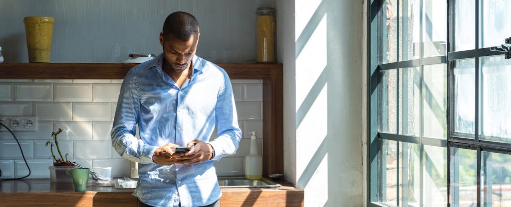 Man standing in his kitchen, reading on his phone