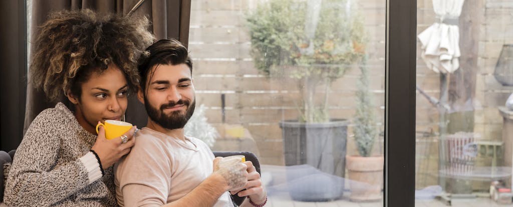 Man and woman sitting together on their couch, drinking coffee and smiling