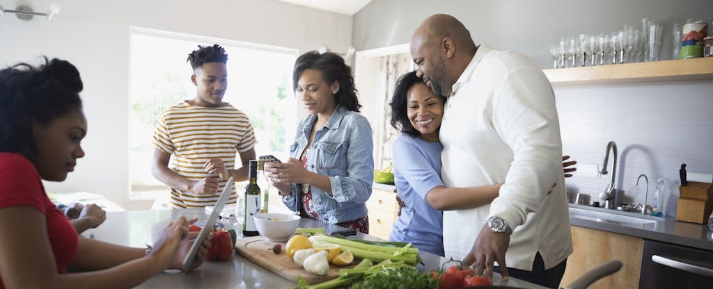 Adult family members standing together in their kitchen, cooking, talking and laughing