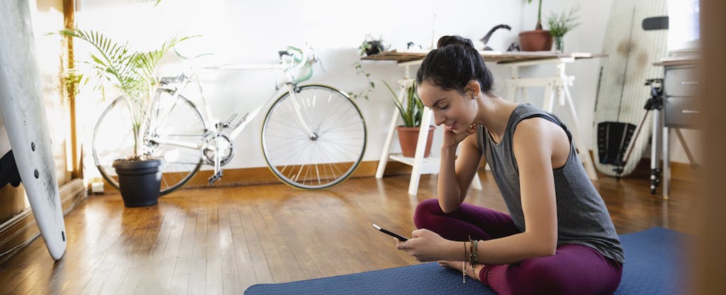 Young woman with smartphone on yoga mat in apartment feeling less anxious about the upcoming tax season