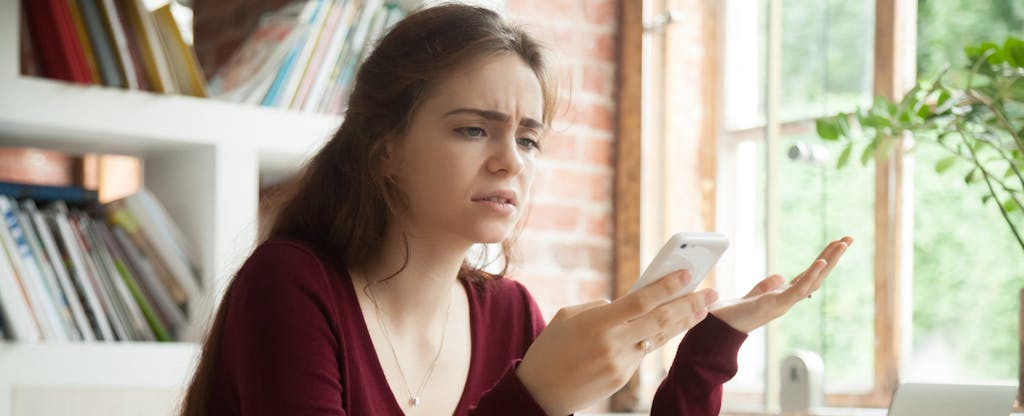 Woman looking at her phone, confused and frustrated