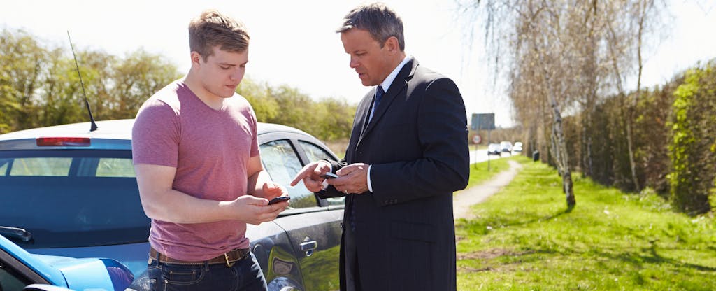 Two men standing next to their cars, exchanging car insurance information after getting into a minor car accident