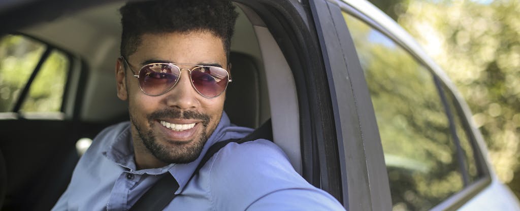 Man wearing sunglasses and sitting in car, thinking about rental car insurance