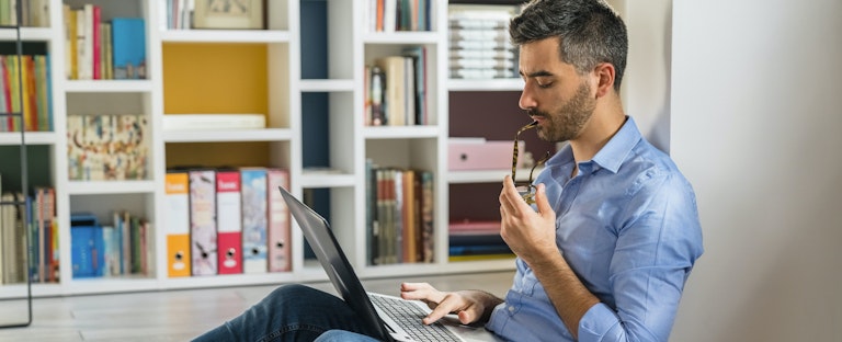 Young man sitting on floor at home, researching cash central loans on his laptop