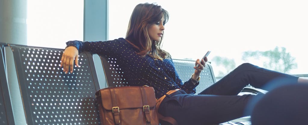 Woman sitting at the airport with her luggage, reading on her phone