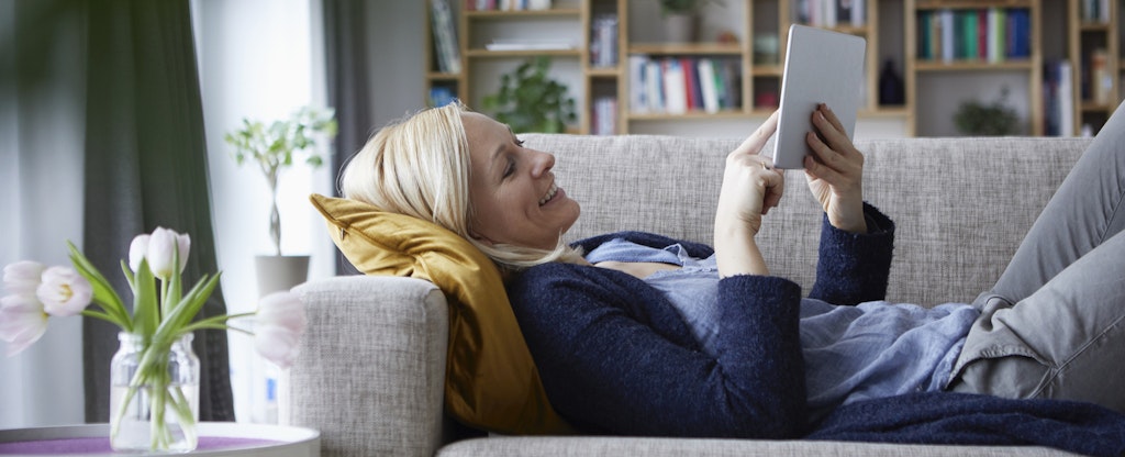 Woman relaxing on her couch, smiling and comparing car insurance rates on her tablet