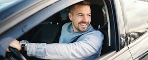 Smiling man in car trying to decide if he needs rental car insurance