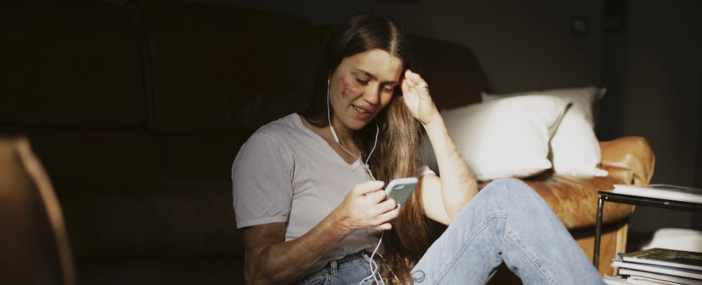 Woman sitting on the floor of her bedroom, reading on her phone about free savings account options