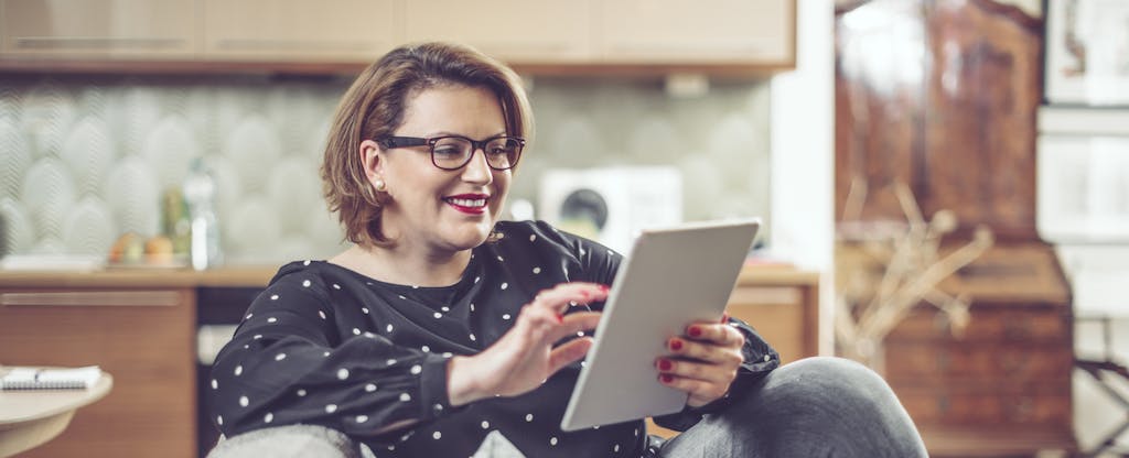 Woman sitting on her couch at home, smiling and reading on her tablet about the best loans for good credit