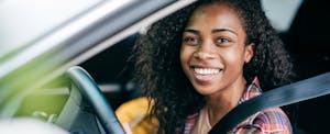 College student sitting in the driver's seat of her car, looking out of the window and smiling