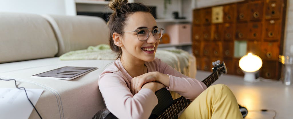 Young woman sitting on her living room floor with her guitar