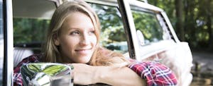 Young woman in a flannel shirt sitting in her car and looking out the window