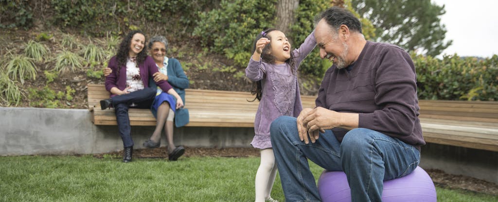 Young child playing in the yard with her grandfather, her mother and grandmother looking on while they discuss setting up an education savings account