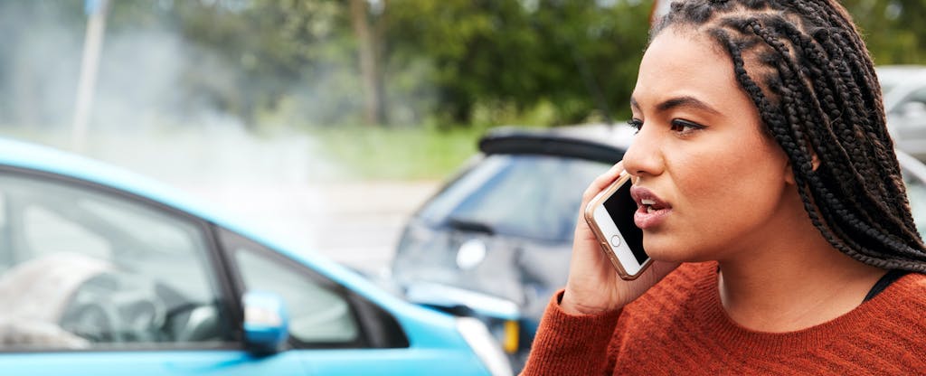 Young woman in a car accident, standing on the side of the road on her phone asking what happens when you total your car