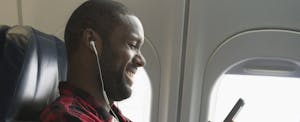 Man sitting near a window on a plane, smiling and reading on his phone about the best airline credit cards