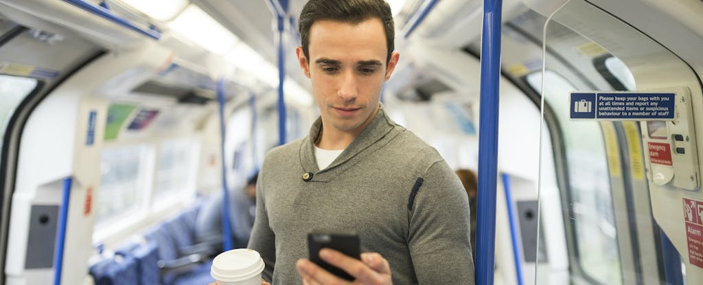 Man standing on train, holding coffee and cell phone and looking up Continental Loans