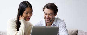 un hombre y una mujer miran una computadora portátil juntos sonriendo