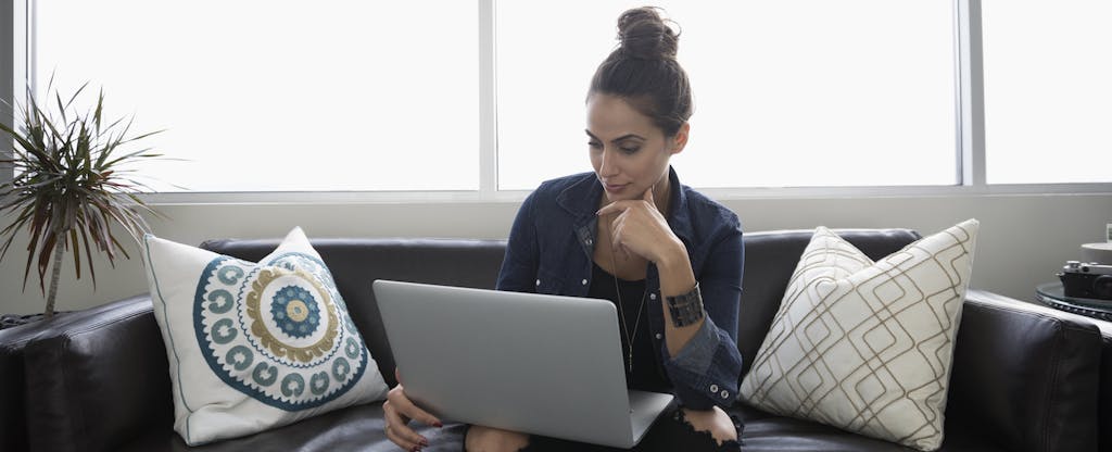 Woman sitting at home on her couch, using her computer to read about how to get tax relief