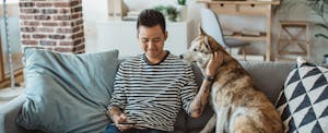 Young man sitting on sofa with his dog and looking up the average credit score on his phone
