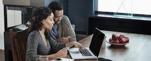 Man and woman sitting together at their kitchen table, looking at a laptop while considering a Credit Direct loan